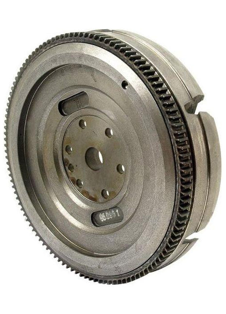 The AGCO Massey Ferguson - Flywheel 12 - 3819666M91 is made of metal with gear teeth around its perimeter, featuring several holes and grooves. Viewed from an angle, it is a crucial component for Massey Ferguson tractors.