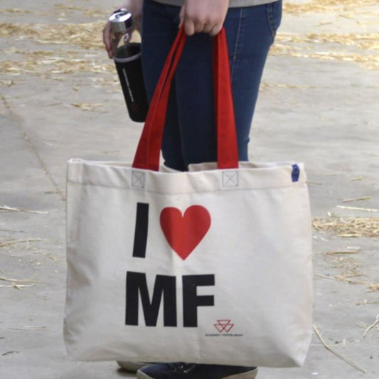 Person holding an AGCO Massey Ferguson shopping bag (Product Code: X993342304000) made of beige cotton with red handles and the text "I ♥ MF" printed on it, while carrying a black drink container.
