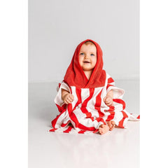 A baby sits on the floor wearing a Massey Ferguson Poncho for Toddlers by AGCO, identified as X993602305000. The red and white striped poncho, made of soft terry cloth, has a red hood that covers the baby's head. The baby appears to be smiling.