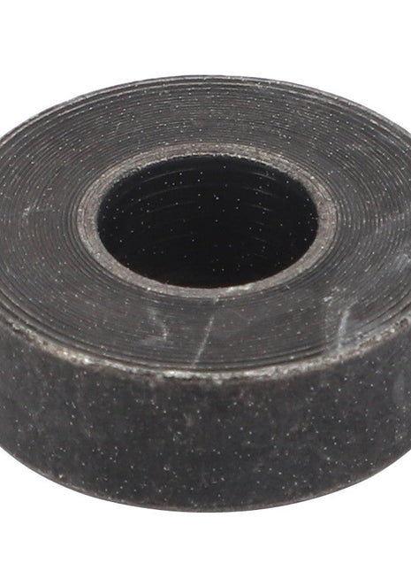 A close-up of a round, flat, black metal washer with a central hole. The surface features circular grooves and has a rough texture. No current product description is available for AGCO | Pipe - F166500030280 by AGCO.