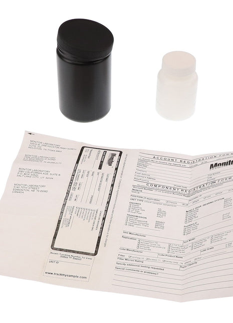 Two AGCO containers from the AGCO KIT - AG715992 are placed neatly above a spread-out document with printed text and tables, one in black and one in white.