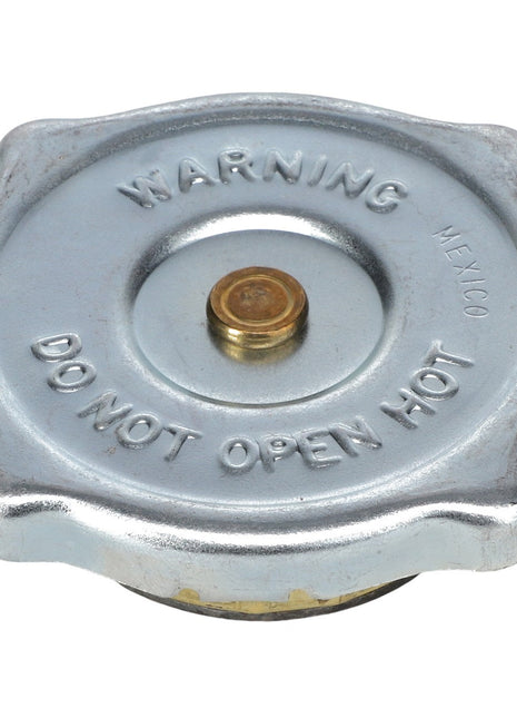 The AGCO | RADIATOR CAP - AG724582 is a metallic AGCO Genuine Radiator Cap with raised lettering that reads "WARNING MEXICO DO NOT OPEN HOT" on the top, designed to maintain cooling system pressure and prevent coolant boiling.