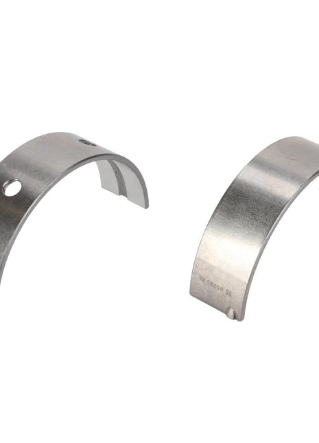 Two semi-circular metallic components, one featuring a hole and the other solid, appear to serve as engine bearings or similar mechanical parts, specifically identified as the AGCO | CRANKSHAFT BEARING - F716201310090 from the AGCO brand.